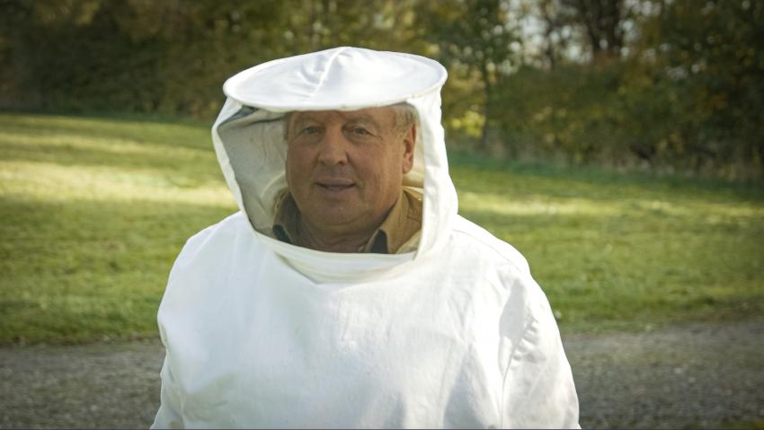Naturtalent Claus Wittmann trägt einen Bienenschutz-Anzug, er lächelt in die Kamera.