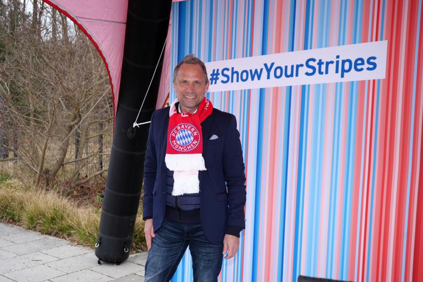 Umweltminister Thorsten Glauber steht vor einer klima.bayern-Klimastreifen-Wand mit dem Hashtag #ShowYourStripes.