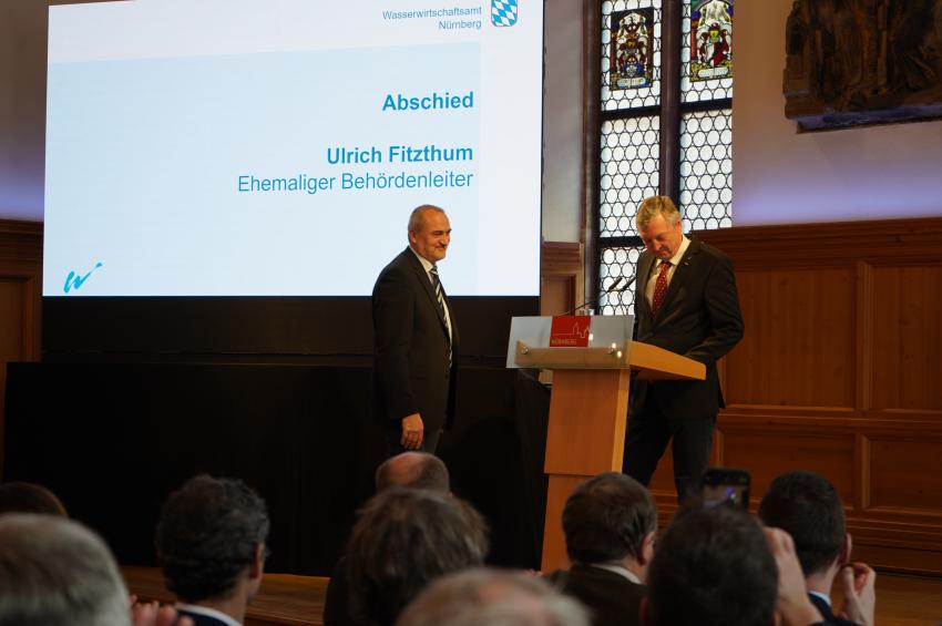 Am Rednerpult steht der bisherige Behördenleiter Ulrich Fitzthum, er verabschiedet sich in den Ruhestand und übergibt das Amt an Herrn Michael Müller (Foto links).