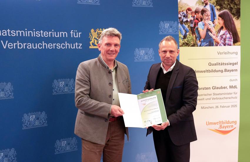 Umweltminister Thorsten Glauber mit einem Vertreter der Naturpark-Umweltstation Waldkirchen, zusammen zeigen sie die Auszeichnungsurkunde.