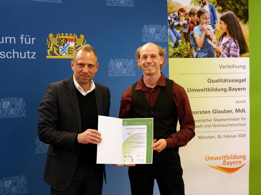Umweltminister Thorsten Glauber mit einem Vertreter des Schullandheimes Thüringer Hütte aus Hausen in der Rhön, zusammen zeigen sie die Auszeichnungsurkunde.