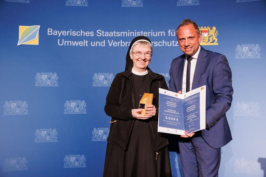 Die Preisträgerin und Umweltminister Thorsten Glauber zeigen zusammen den Klimaschutzpreis und die Urkunde.