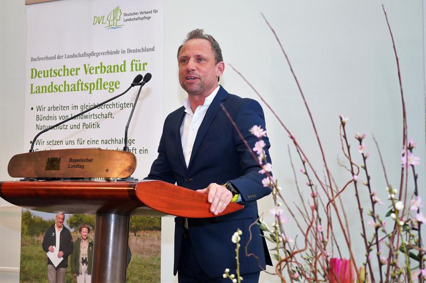 Am Rednerpult steht der bayerische Umweltminister Thorsten Glauber und spricht ein Grußwort an alle Teilnehmer der Veranstaltung des Deutschen Verband für Landschaftspflege (DLV) 