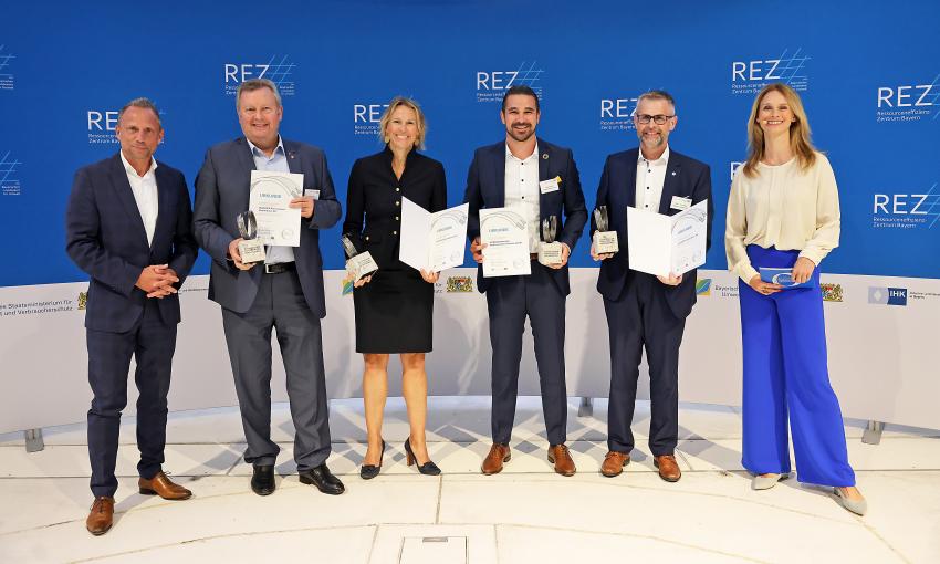 Das Gruppenfoto zeigt den Bayerischen Staatsminister für Umwelt und Verbraucherschutz, Thorsten Glauber (links) zusammen mit den diesjährigen Gewinnern des Bayerischen Ressourceneffizienzpreises und Berenike Beschle (Moderatorin).
