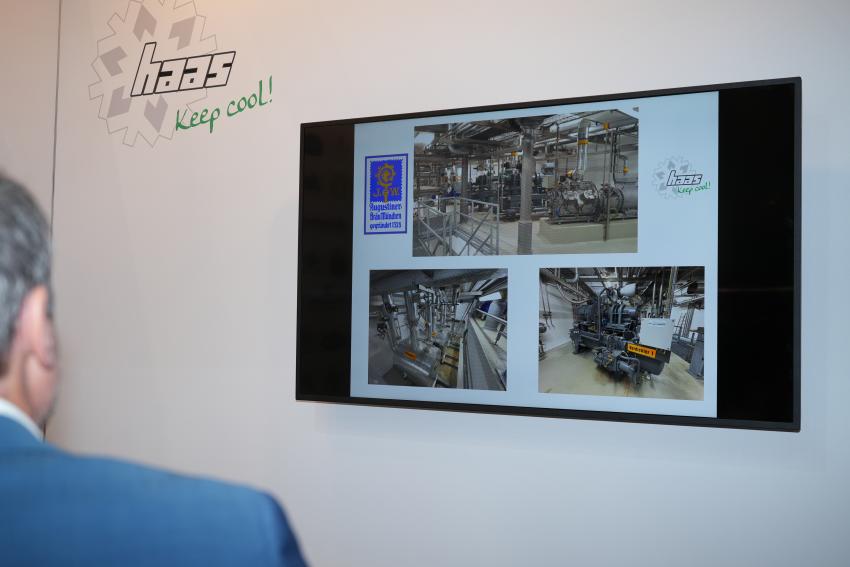 Umweltminister Thorsten Glauber schaut auf ein Wandbild mit Fotos der Firma Haas Kälteanlagen in Messehalle 9.