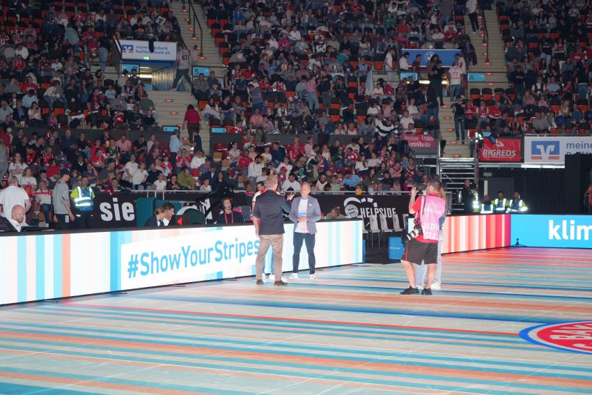Umweltminister Thorsten Glauber führt in der Halbzeitpause ein Interview mit dem Stadionsprecher und einem Vertreter des FC Bayern Basketball