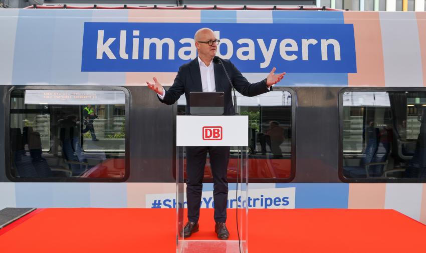 Heiko Büttner (DB-Konzernbevollmächtigter für den Freistaat Bayern) steht vor dem Klimastreifenzug am Rednerpult.