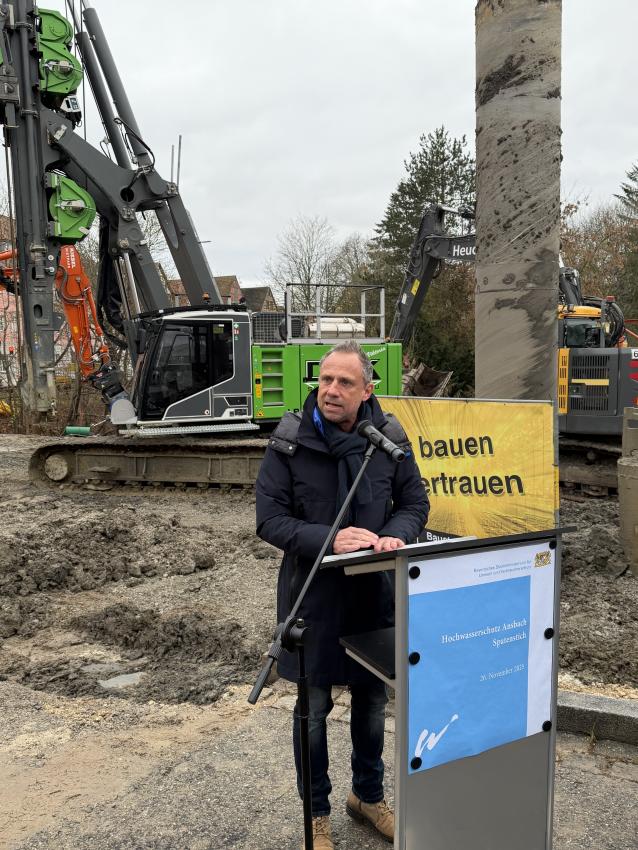 Auf der Baustelle am Rednerpult steht Minister Glauber und hält eine Rede.