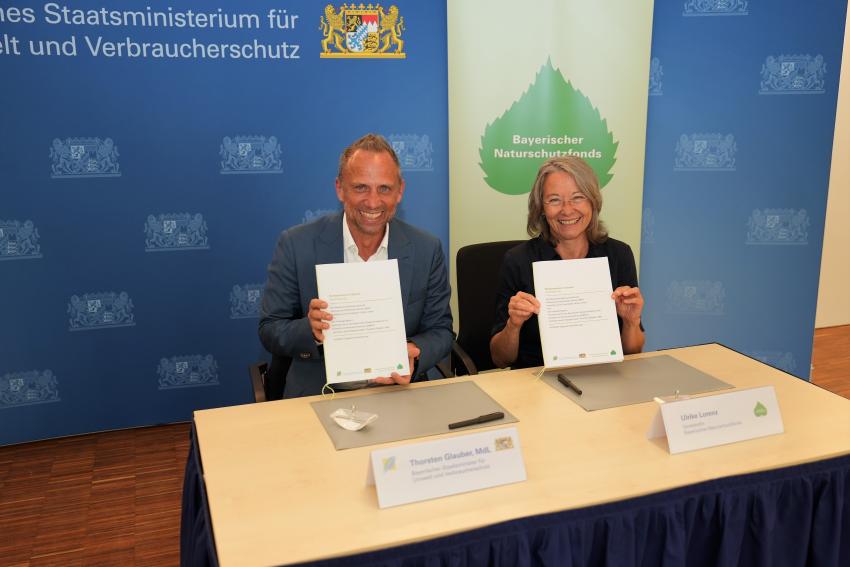 Umweltminister Thorsten Glauber und Frau Ulrike Lorenz (Vorständin des Naturschutzfonds) unterzeichnen die Vereinbarung zum Biotopverbund in Bayern.