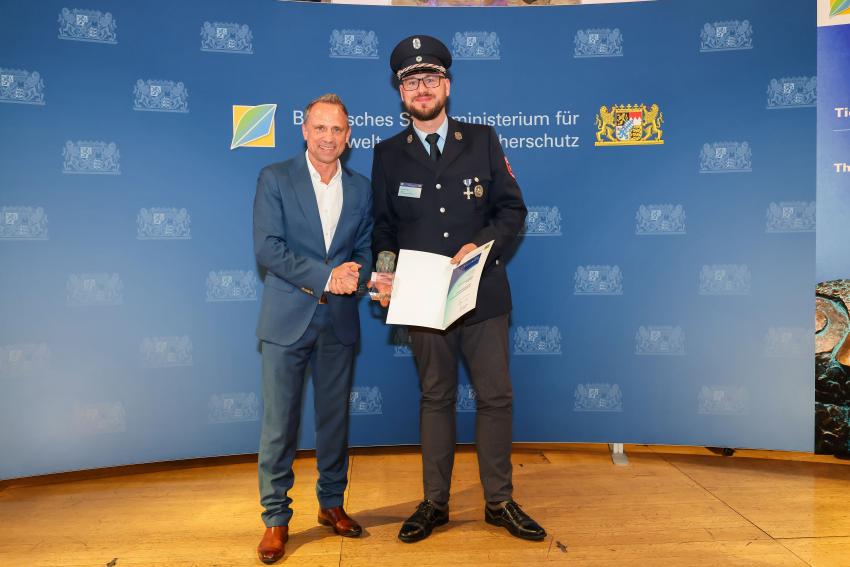 Das Foto zeigt den Bayerischen Umweltminister Thorsten Glauber mit einem Vertreter der Freiwilligen Feuerwehr Sindelbach, die Auszeichnungsurkunde und den Tierschutzpreis.