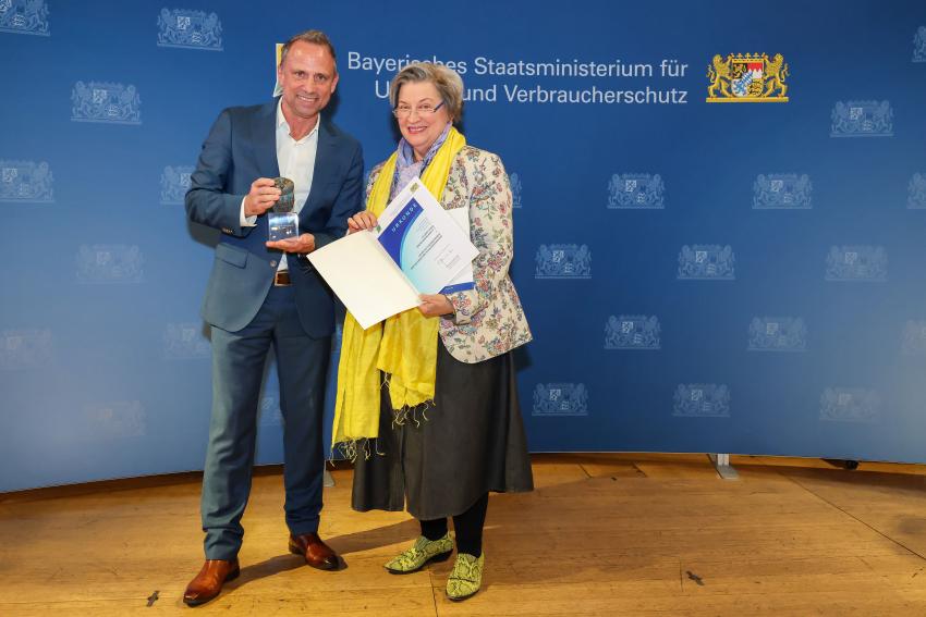 Das Foto zeigt den Bayerischen Umweltminister Thorsten Glauber mit einer Vertreterin der Kitzrettung Dreiburgenland e. V., die Auszeichnungsurkunde und den Tierschutzpreis.