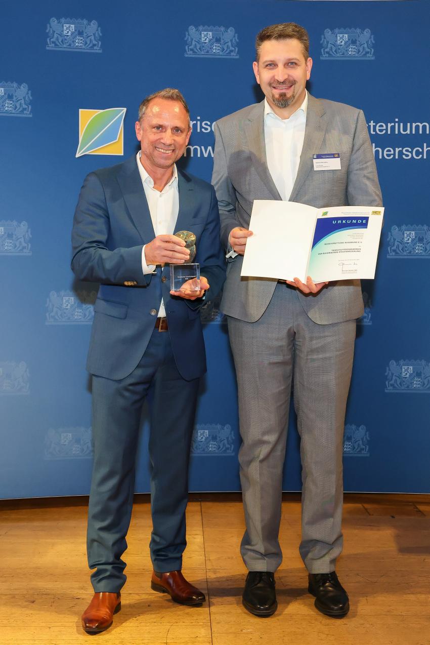Das Foto zeigt den Bayerischen Umweltminister Thorsten Glauber mit einem Vertreter der Rehkitzrettung Augsburg e. V., die Auszeichnungsurkunde und den Tierschutzpreis.