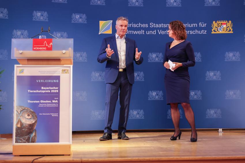 Auf der Bühne steht Festredner Hannes Jeanicke (Tierschützer, Umweltaktivist und Schauspieler) und die Moderatorin Barbara Siebert (StMUV).