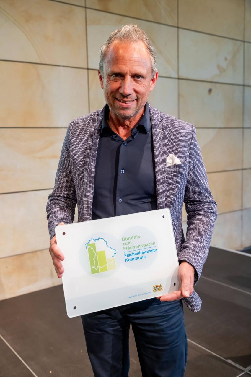 Minister Glauber mit dem Schild Flächenbewusste Kommune