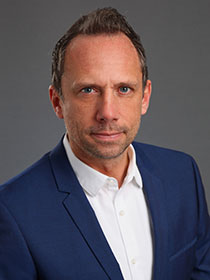 Portrait des Umweltministers Thorsten Glauber im Anzug vor grauem Hintergrund