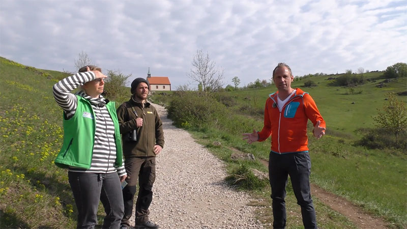 Das Bild zeigt Umweltminister  Thorsten Glauber im Gespräch mit Jana Wiehn (Gebietsbetreuerin im Landschaftspflegeverband Forchheim) und Johannes Stemper (Ranger im Naturpark Fränkische Schweiz) sitzend auf einer Bank auf dem Walberla