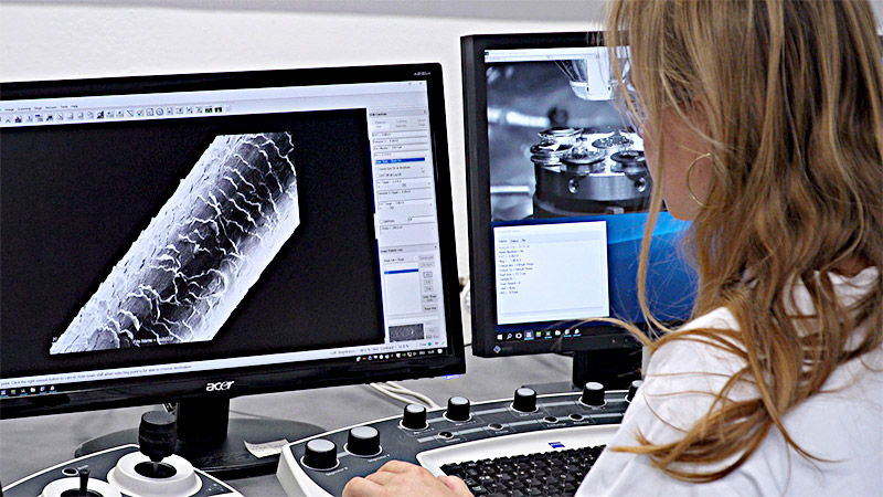 Das Bild zeigt eine Schülerin, die auf einem Bildschirm die Elektronenmikroskopaufnahme eines menschlichen Haares betrachtet