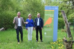 Herr Staatsminister Glauber (links) neben Rotraud Krüger und Dr. Norbert Schäffer in einem grünen Garten neben einem Rollup vogelfreundlicher Garten.