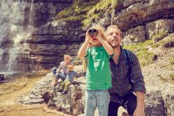 Eine Familie bei einem Ausflug in felsigem Gelände, vorne Vater mit Sohn, der durch ein Fernglas schaut.