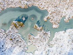 Luftbild eines mäandrierenden Baches in einer Schneelandschaft