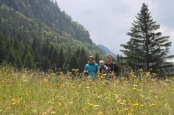 Eine Bergwiese im Hintergrund steht eine Familie: Ehepaar und zwei Kinder