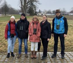 Fünf Personen, drei davon mit Fernglas, sehten auf einer Wiese und blicken in die Kamera.