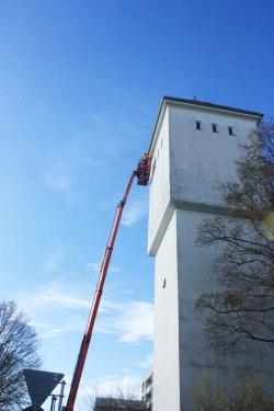 Eine Teleskopleiter ist einen hohen Wasserturm hochgefahren, oben arbeiten zwei Personen.