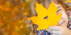Ein Mädchen blickt zur ein herzförmig in ein herbstliches Ahornblatt geschnittenes Loch,