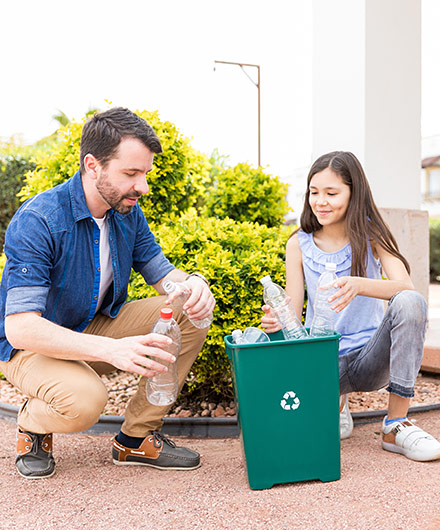 Das Bild zeigt einen Mann und eine Frau vor einem Mülleimer auf dem ein Recyclingsymbol ist