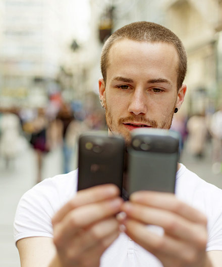 Das Bild zeigt einen Mann, der auf 2 Smartphones schaut